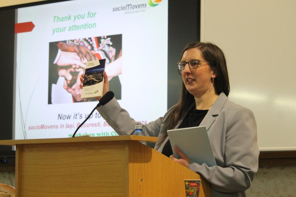Claudia Schwarz am Redepult mit Flyer von socioMovens